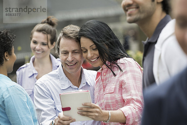 Menschen im Frühling in der Stadt im Freien. New York City. Eine Gruppe von Männern und Frauen  in der Mitte ein Paar  das auf einen digitalen Tablet-Bildschirm schaut.