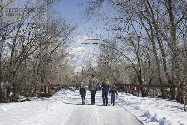 Winterlandschaft mit Schnee auf dem Boden. Eine Familie  Erwachsene und zwei Kinder  die eine leere Straße entlanglaufen.