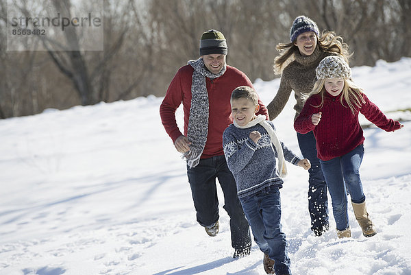 Winterlandschaft mit Schnee auf dem Boden. Familienspaziergang. Zwei Erwachsene auf der Jagd nach zwei Kindern.