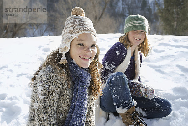 Winterlandschaft mit Schnee auf dem Boden. Eine Frau und ein Kind sitzen lachend auf dem Boden.