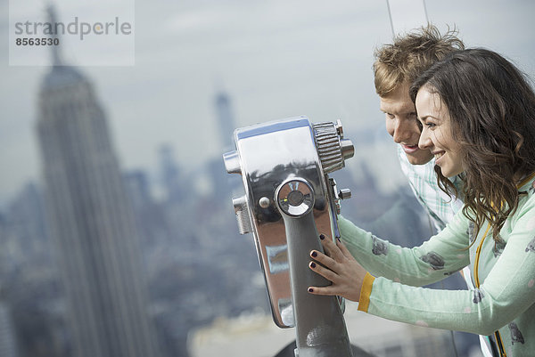 New York City. Eine Aussichtsplattform mit Blick auf das Empire State Building. Ein junges Paar schaut durch das Teleskop.