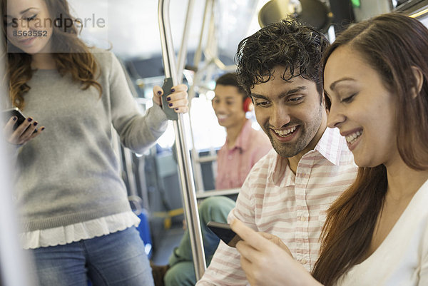 Urbaner Lebensstil. Eine Gruppe von Menschen  Männer und Frauen  in einem Stadtbus in New York City. Ein Mann mit Kopfhörern und ein Paar  das sich ein Mobiltelefon ansieht.