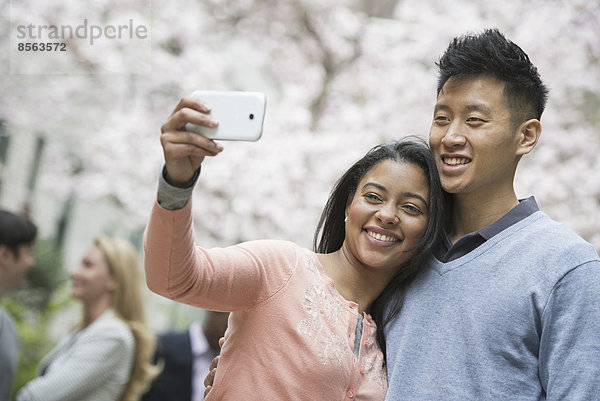 Stadtleben im Frühling. Jugendliche im Freien in einem Stadtpark. Ein Paar beim Selbstporträt oder Selbstporträt mit einem Smartphone.