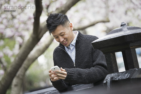 Stadtleben im Frühling. Ein junger Mann im Freien in einem Stadtpark. Sitzt auf einer Bank.