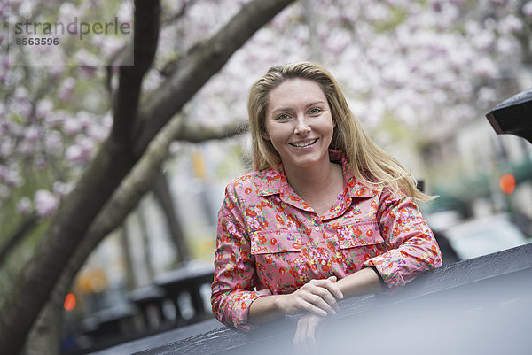 Stadtleben im Frühling. Eine junge Frau mit langen blonden Haaren  draußen in einem Stadtpark.