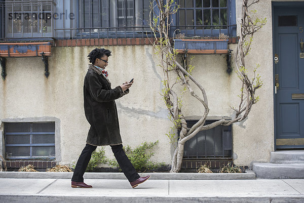 Eine Frau in einem warmen Mantel geht die Straße entlang und überprüft ihr Telefon.