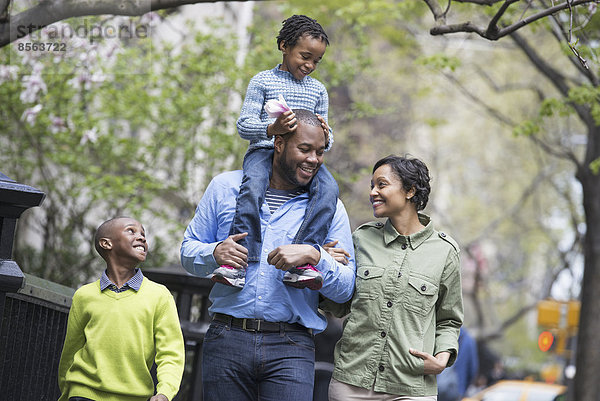 Ein New Yorker Stadtpark im Frühling. Eine Familie  Eltern und zwei Jungen. Ein Kind  das auf den Schultern seines Vaters reitet.
