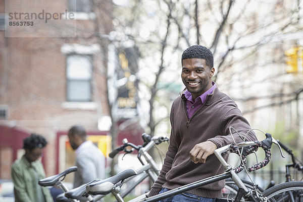 Draußen in der Stadt im Frühling. Ein urbaner Lebensstil. Ein junger Mann  der in die Kamera lächelt. Fahrradständer.