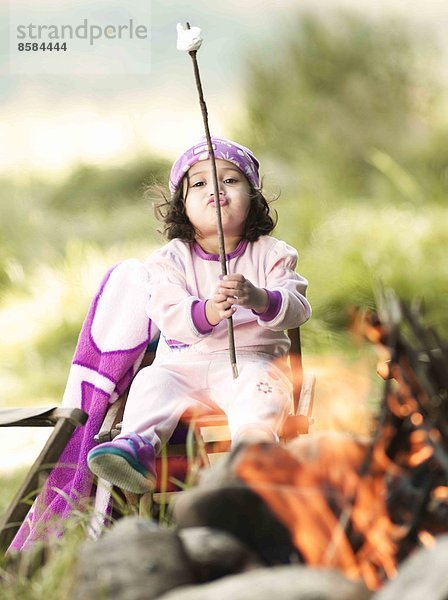 Kleines Mädchen lächelt und macht Gesichter  in der Nähe von Feuer im Freien.