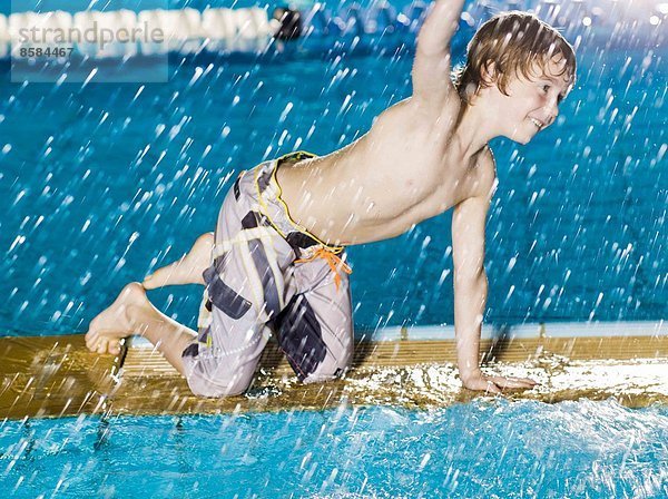 Junge spritzt Wasser am Rande des Schwimmbades