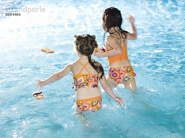 Zwei Mädchen laufen im Wasser am Schwimmbad  von hinten gesehen