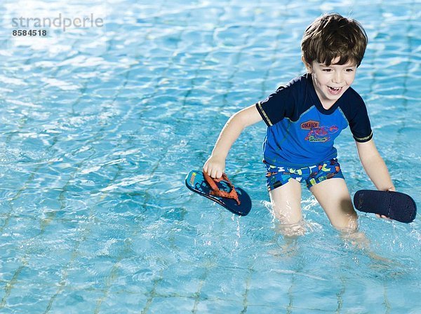 Junge spielt mit seinen Sandalen im Schwimmbad