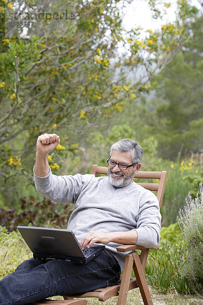 Mann im Garten sitzend mit Laptop  lächelnd  Brille tragend