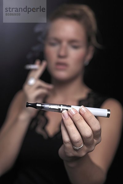 Frankreich  junge Frau raucht und hält elektronische Zigarette.