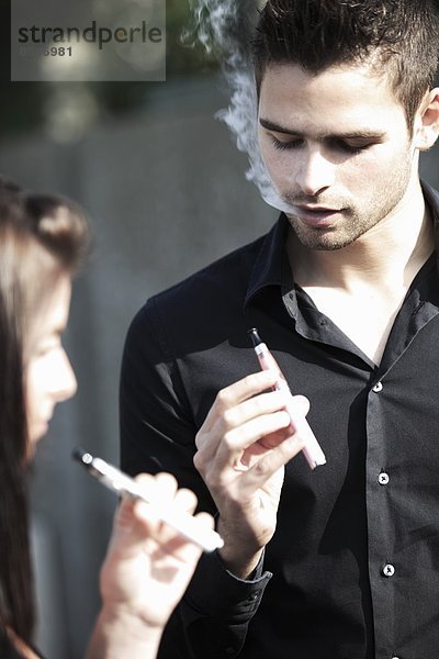 Frankreich  junges Paar  das elektronische Zigaretten raucht.