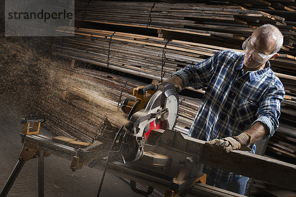 Eine zurückgewonnene Holzwerkstatt. Ein Mann mit Schutzbrille  der mit einer Kreissäge Holz sägt.