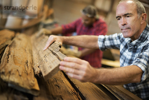 Eine zurückgewonnene Holzwerkstatt. Eine Gruppe von Menschen  die arbeiten. Ein Mann misst und kontrolliert Holzbretter zur Wiederverwendung und zum Recycling.