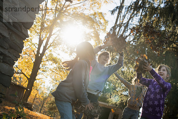 Drei Kinder in der Herbstsonne. Spielen im Freien und werfen die abgefallenen Blätter in die Luft.