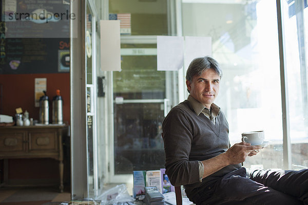 Ein Mann sitzt in einem Café. Er hält eine Tasse schaumigen Cappuccino-Kaffee in der Hand.