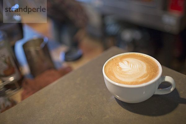 Coffee-Shop-Tisch. Eine volle Tasse Kaffee aus weißem Porzellan mit aufgeschäumter Milchauflage.