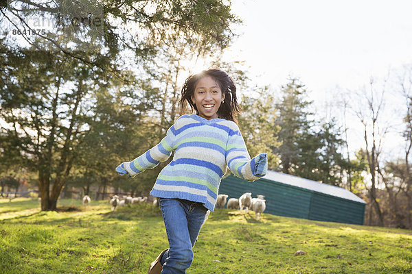 Ein junges Mädchen in einem blau gestreiften Top läuft auf einem Schafsfeld in einem Tierschutzgebiet.