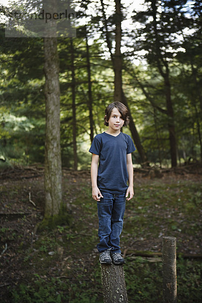 Ein Junge steht auf einem schmalen Baumstamm  balanciert und geht über die Planke.
