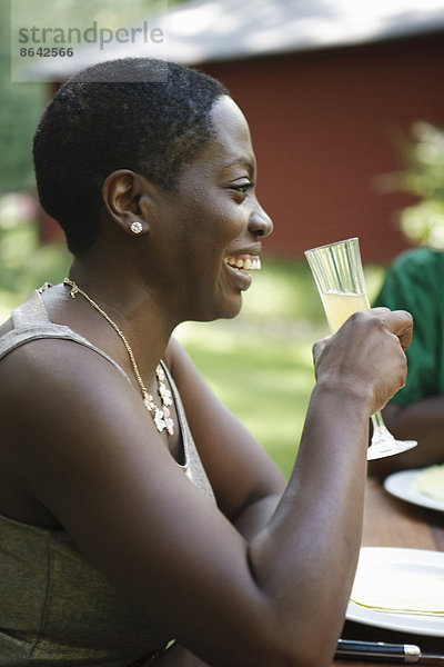 Eine Frau sitzt an einem Tisch im Freien in einem Garten und nimmt einen Drink zu sich.