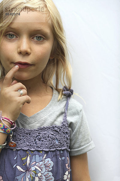 Ein junges Mädchen mit blonden Haaren und blauen Augen. Die Hand zum Mund.