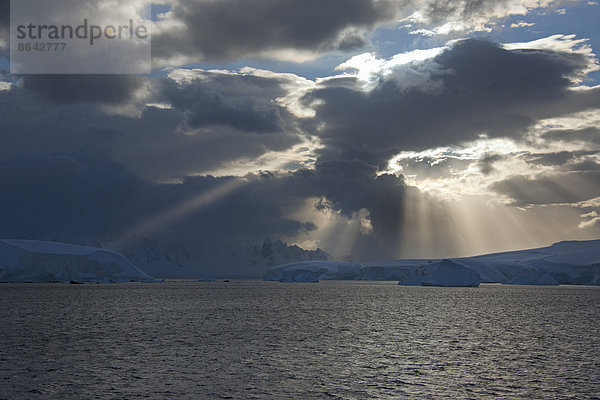 Die Sonne durchbricht die Sturmwolken und trifft auf die Eisberge entlang der Westküste der Antarktischen Halbinsel.