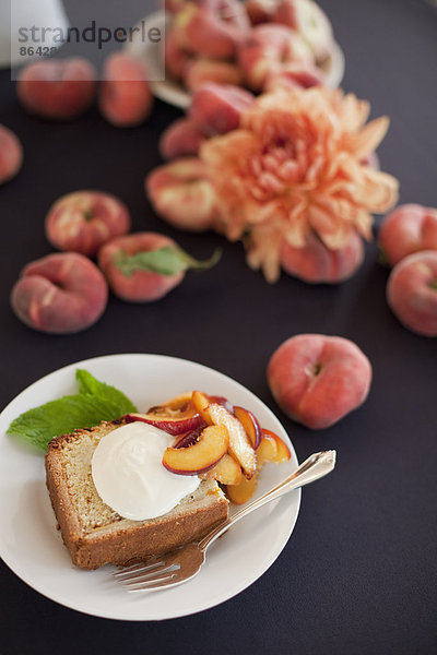 Frisches Obst und Blumen. Ein Stück Bio-Pfirsichkuchen mit einer Portion Creme fraiche und Donut-Pfirsichen.