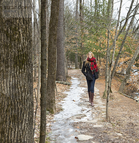 Eine Frau in einem Wintermantel und mit rotem Schal  die im Winter einen Waldweg hinuntergeht.