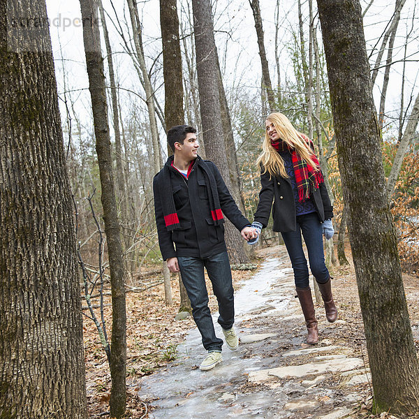 Ein Paar  das im Winter Hand in Hand durch ein Waldgebiet läuft.