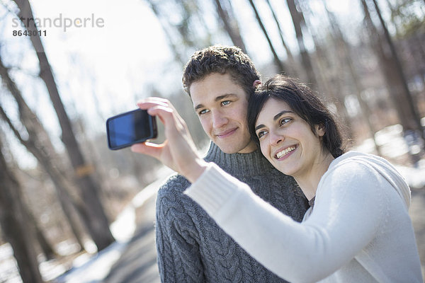 Ein Paar im Freien an einem verschneiten Tag. Frau hält ein Fotohandy in der Hand und fotografiert in Armlänge.