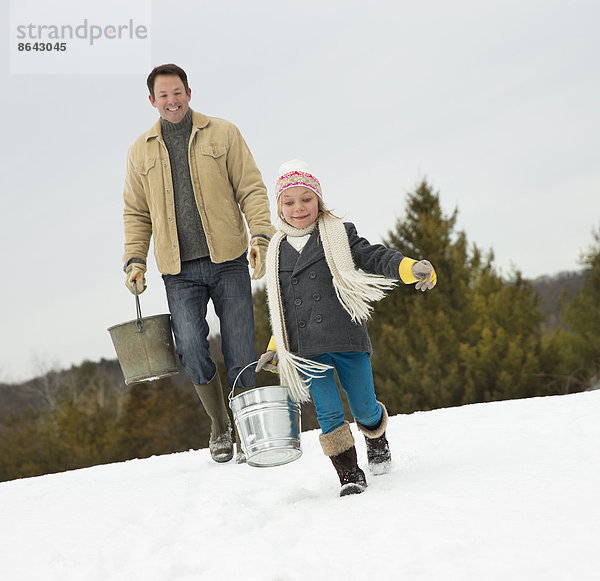 Ein Mann und ein Kind mit Eimern  die durch den Schnee rennen.