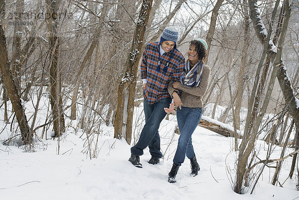 Winterlandschaft mit Schnee auf dem Boden. Ein Paar  das Arm in Arm durch den Wald geht.