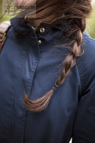 Eine Frau mit langen braunen Haaren  die zu einem Zopf geflochten sind. Sie trägt eine blaue Lederjacke. Nahaufnahme.