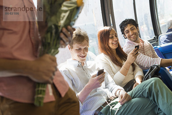 Urbaner Lebensstil. Eine Gruppe von Menschen  Männer und Frauen  in einem Stadtbus in New York City. Zwei Personen überprüfen ihre Telefone. Ein Mann steht mit einem Blumenstrauß in der Hand.