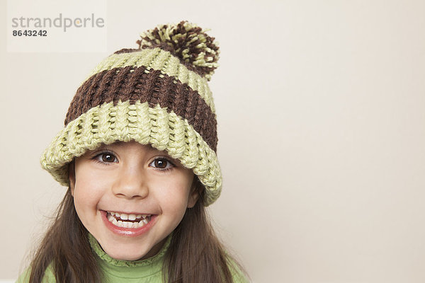 Ein kleines Kind mit langen braunen Haaren  das eine Strickmütze mit Pompon trägt.