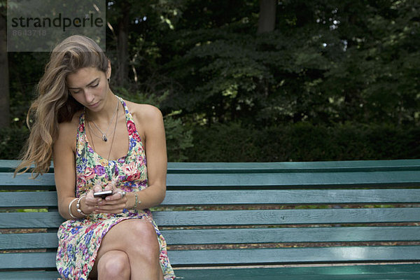 Junge Frau sitzt auf der Parkbank mit dem Handy
