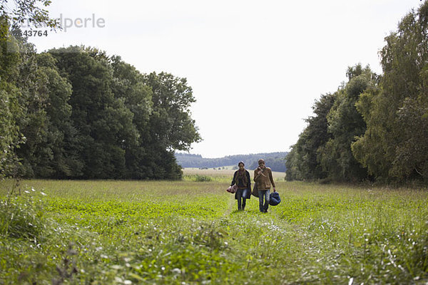 Junges Paar mit Campingaccessoires beim Spaziergang durchs Feld