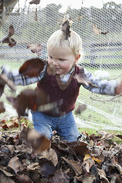 Baby Junge wirft trockene Blätter