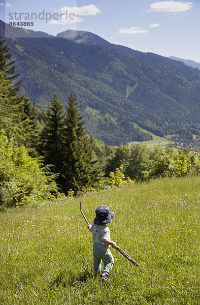 Kleiner Junge hält Stock und geht auf Feld