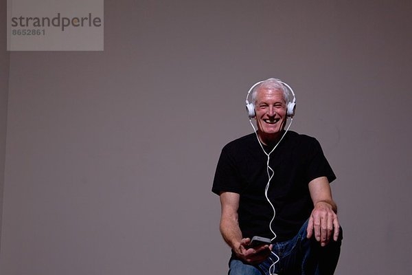 Porträt eines älteren Mannes  der den MP3-Player über Kopfhörer hört.