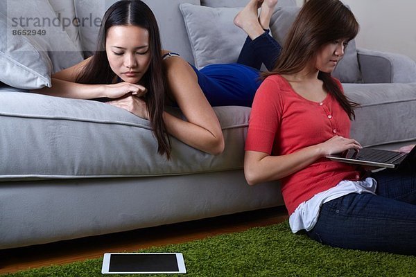Zwei junge Frauen im Wohnzimmer mit digitalen Tabletten