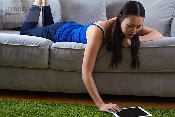 Junge Frau auf dem Sofa mit digitalem Tablett