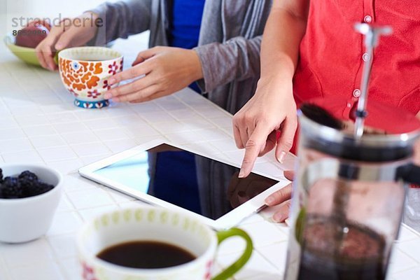 Zwei junge Frauen in der Küche mit digitaler Tablette beim Kaffeetrinken