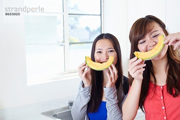 Zwei junge Frauen in der Küche mit Melonen-Smiley-Gesichtern