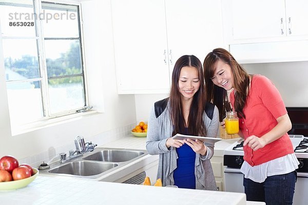 Zwei junge Frauen in der Küche beim Betrachten des digitalen Tabletts