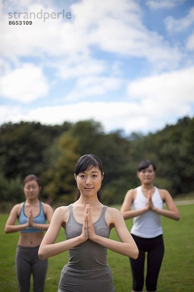 Drei junge Frauen im Park praktizieren Yoga