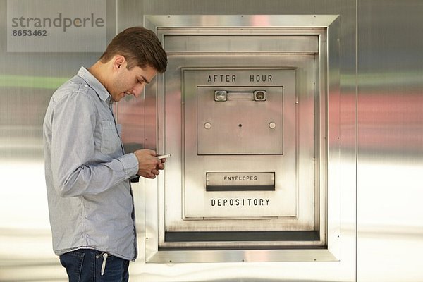 Mittlerer Erwachsener Mann  der auf dem Handy neben dem Bankschließfach sitzt.